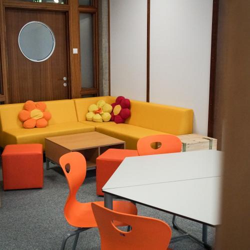 Blick in die Sitzecke der Bibliothek, zu sehen ist eine gelbe Couch mit rot-orangen Blumen-Polster